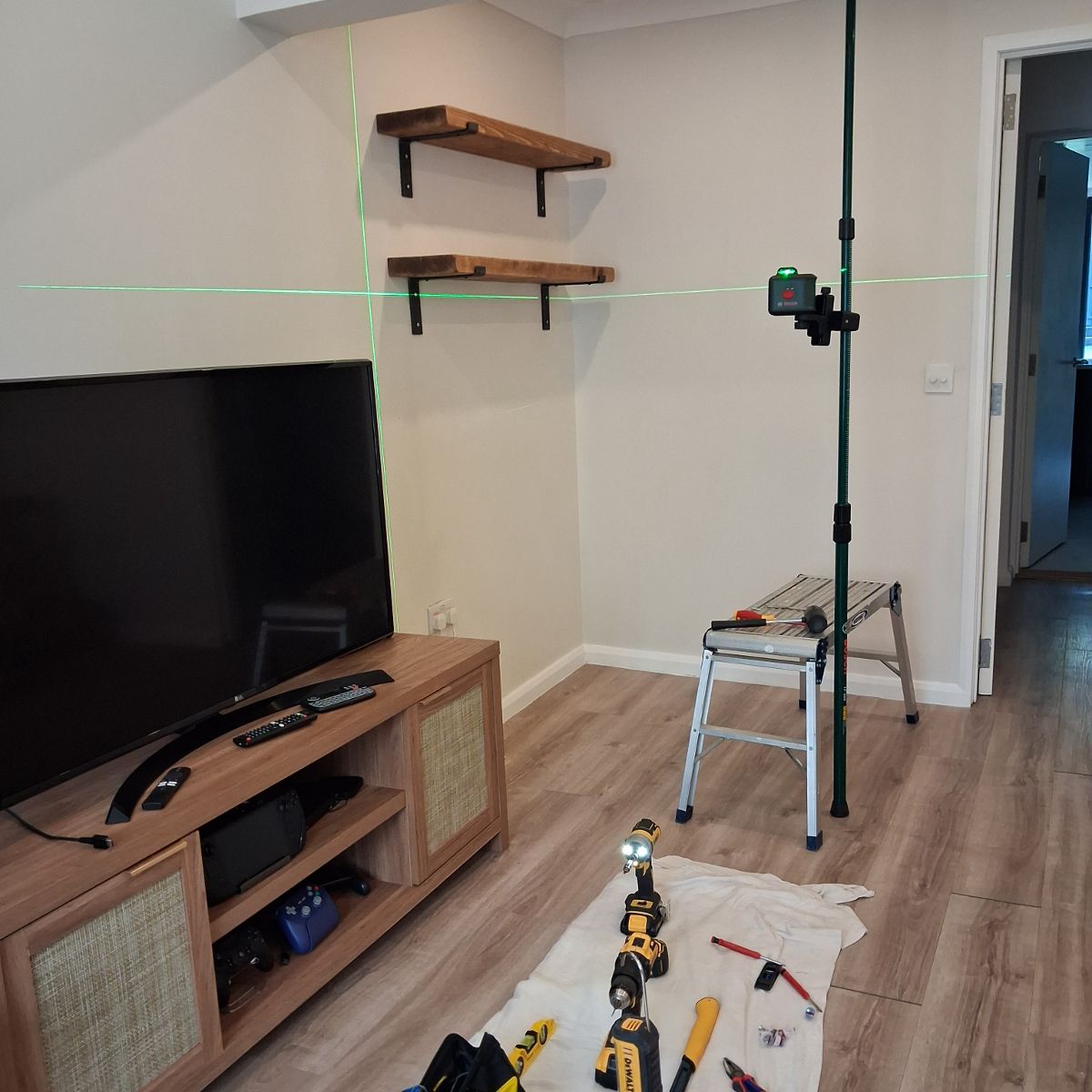 Before: a television on a low unit below an empty wall, laser level set up